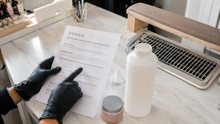 Nail technician reviewing safety data beside closed salon products and local exhaust ventilation